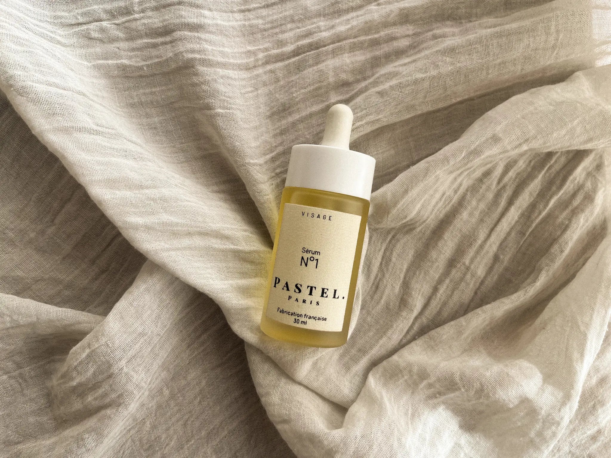 Sérum N°1 PASTEL.PARIS, flacon compte-gouttes posé sur un tissu en lin froissé